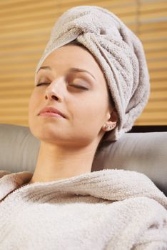 Woman in bathrobe relaxing at spa with eyes closed.