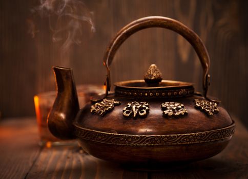 Antique iron hot tea pot fuming on dark wooden background