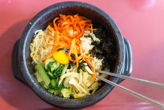 Bibimbap in a heated stone bowl, a signature korean dish with egg and fresh vegetables