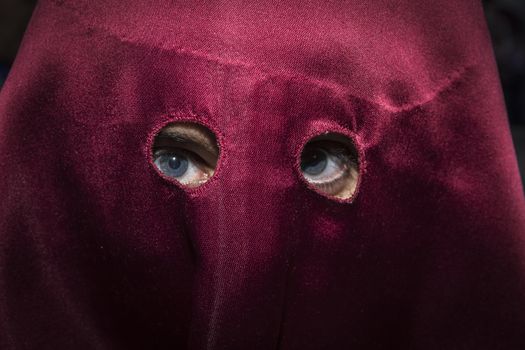 Detail of blue eyes of penitent with caperuz red during Holy Week in Spain