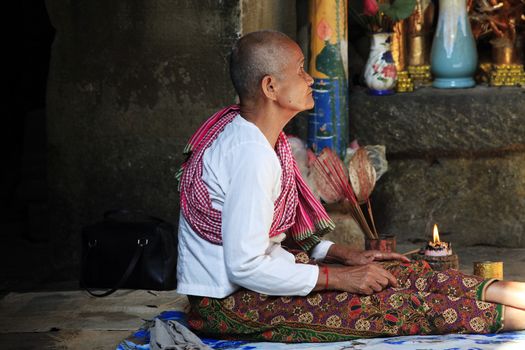 SIEM REAP, CAMBODIA - APRIL 06: Old wrinkled traditional Asian woman praying with incense sticks inside a temple in Siem Peap 06 April, 2014. Cambodia