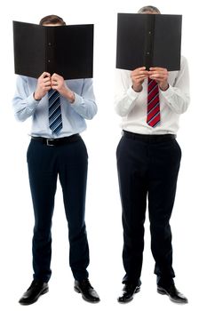 Two male executives hiding face behind a file folder
