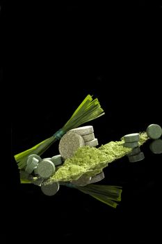 Green dietary supplements. Pills, ground powder, effervescent pills of chlorella, spirulina, wheat grass and barley grass isolated on black background. Detox, natural healthy alternative medicine. 