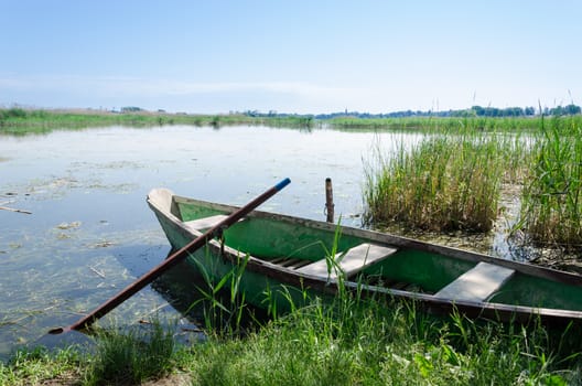 old boat scratched paint with oars to high grass covered coast spring time