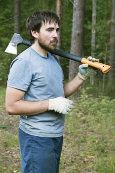 Young lumberman in a forest with an axe on his shoulder 