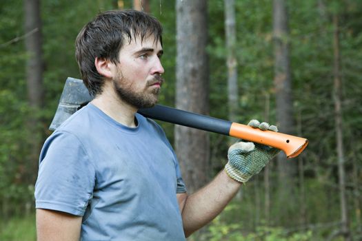 Young lumberman in a forest with an axe on his shoulder 