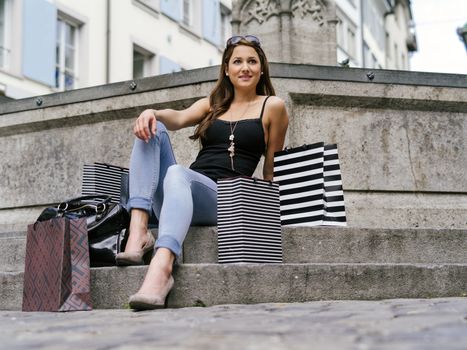 Photo of a beautiful young woman sitting with her shopping bags at a fountain in an old European city resting.