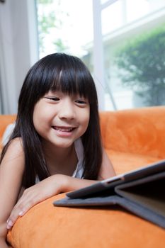 Girl playing with tablet. Lying on the orange sofa at home.