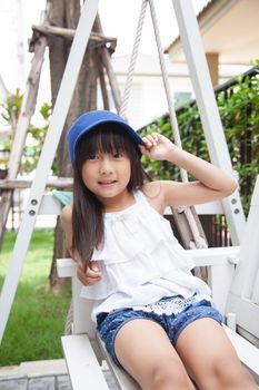 girl sitting on a swing. hand holding blue hat. Smiling and laughing