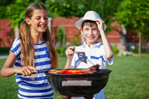 Happy kids preparing meat and vegetables using a barbecue grill