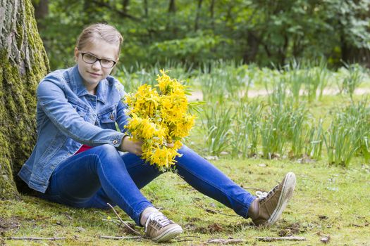 Smiling girl with big bouquet of spring flowers sitting in the park