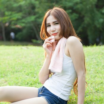 Woman sitting tired after jogging. Located on the lawn in the park.