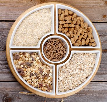 Various Muesli, Oat Flakes and Bran in White Plates closeup on Wooden background. Top View