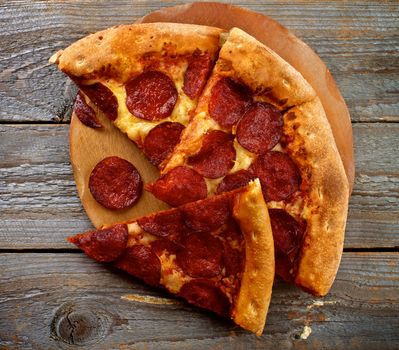 Tasty Pepperoni Pizza with Slice of Salami on Wooden Plate closeup on Rustic Wooden background. Top View