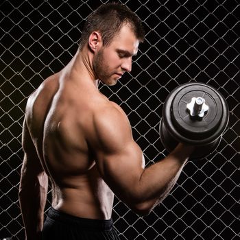 Beautiful, strong man with a dumbbell on fence background