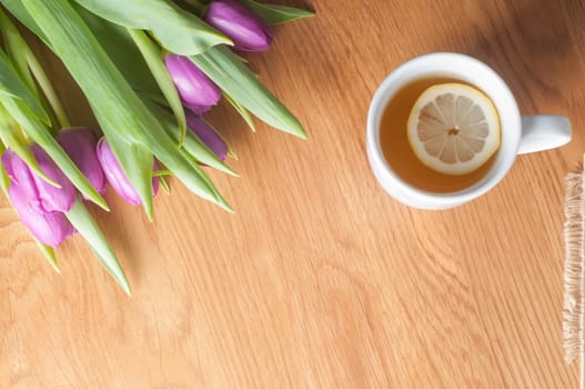 Fresh violet tulips and tea cup on the wooden table
