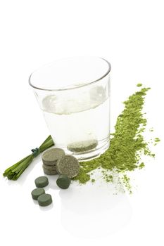 Green effervescent tablet dissolving in glass of water. Spirulina, chlorella, wheatgrass and barley grass isolated on white background. Alternative medicine.