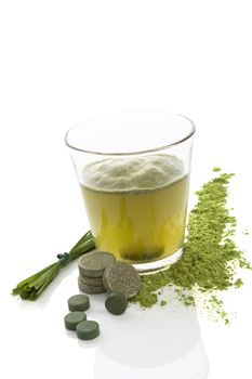 Green juice. Dietary supplements, spirulina, chlorella, wheatgrass tablets, pills and blades of grass isolated on white background. Healthy living, alternative medicine.