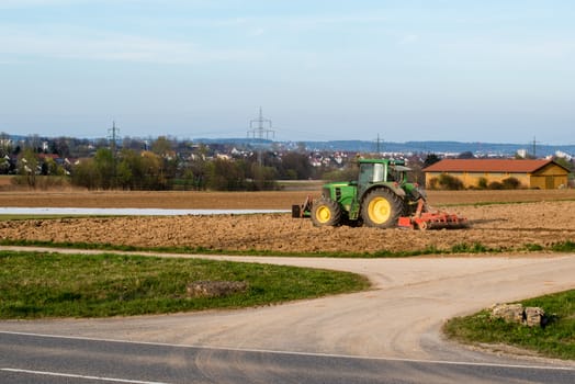 A tractor plowing a field with farm and village in the background