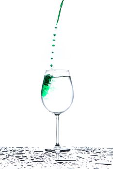 Glass with flowing stream and drops of green water