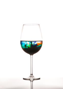 Glass with multicolored water on white background, concept of polution