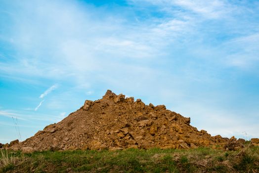 A pile of dirt and rubble at a construction site on green grass with great blue sky