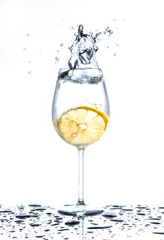 Lemon splashing into glass full of water on white background
