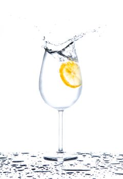 Lemon splashing into glass full of water on white background