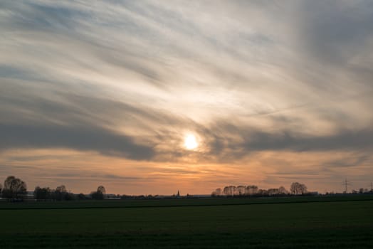 Dramatic and beautiful spring sunset view with trees, meadows and a city in the background