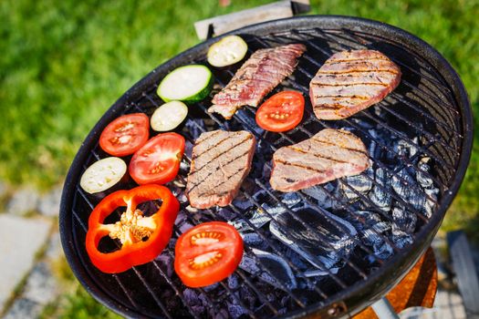 Barbecue on a hot day during the summer vacation on a green grass background. Meat and vegetables on the grill.