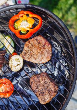 Barbecue on a hot day during the summer vacation on a green grass background. Meat and vegetables on the grill.