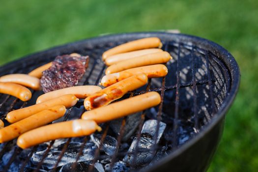 Fresh sausage and hot dogs grilling outdoors on a barbecue grill.