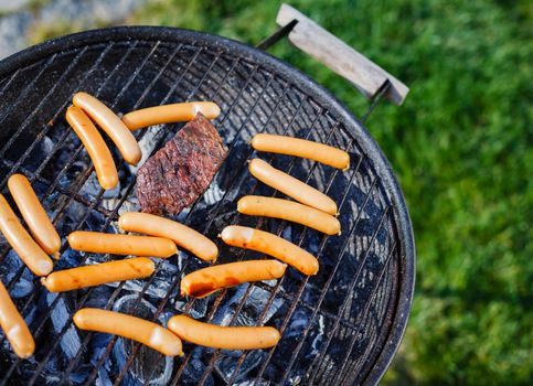 Fresh sausage and hot dogs grilling outdoors on a barbecue grill.