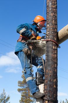 Electrician working on electricity pylon chainsaw against the blue sky 