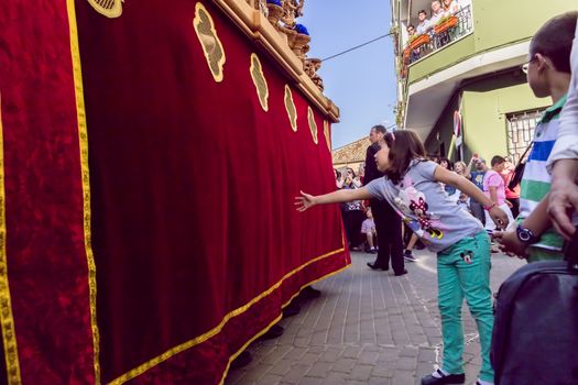 Linares, Jaen province, SPAIN - March 17, 2014: Girl tries to touch the skirt of the throne to have good luck, popular tradition in Andalusia, Easter procession on Holy Thursday, taken in Linares, Jaen province, Andalucia, Spain