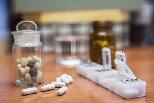 Old bottle of pills along with a few pills above a wooden table