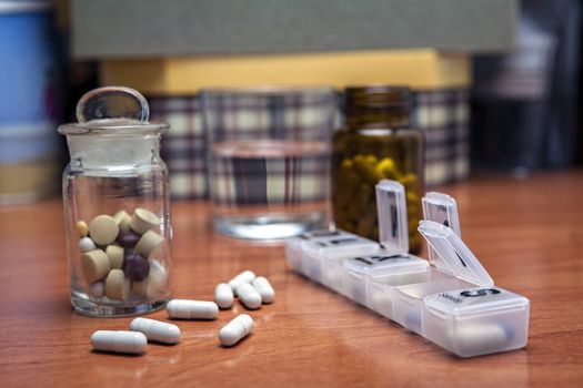 Old bottle of pills along with a few pills above a wooden table