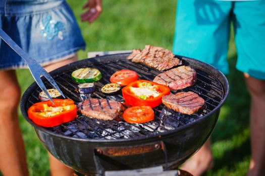 Barbecue on a hot day during the summer vacation on a green grass background. Meat and vegetables on the grill.