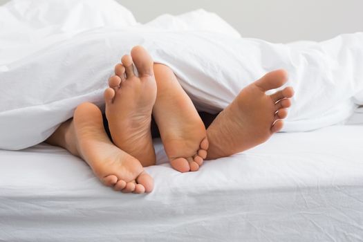 Couples feet sticking out from under duvet at home in bedroom