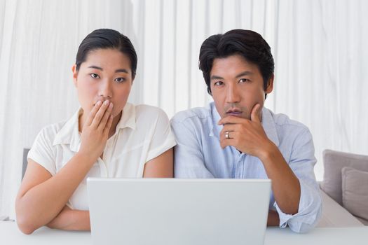 Worried couple using laptop together at home in the living room