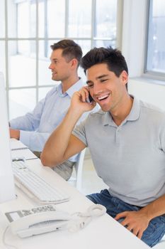 Casual businessman laughing on the phone at his desk in the office