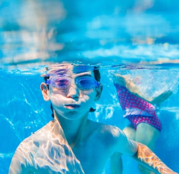 The cute boy swimming underwater in swimming goggles