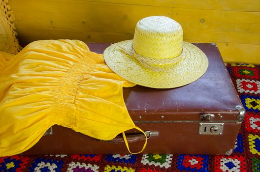 girly yellow summer dress and straw hat lying on an antique large suitcase