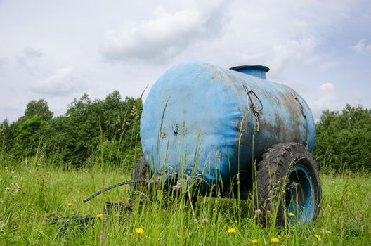 Blue water cistern for animal stand between pasture grass and clovers move in wind.