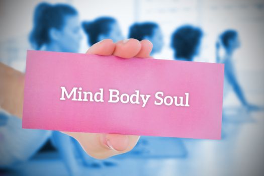 Woman holding pink card saying mind body soul against yoga class in gym