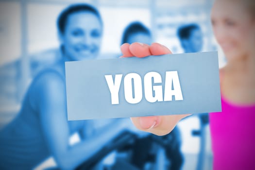 Fit blonde holding card saying yoga against spinning class in gym 