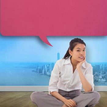 Businesswoman sitting cross legged with speech bubble thinking against city projection on wall