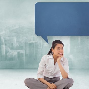 Businesswoman sitting cross legged with speech bubble thinking against city scene in a room