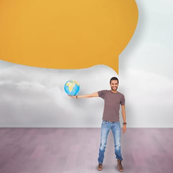 Handsome man holding out a globe with speech bubble against clouds in a room