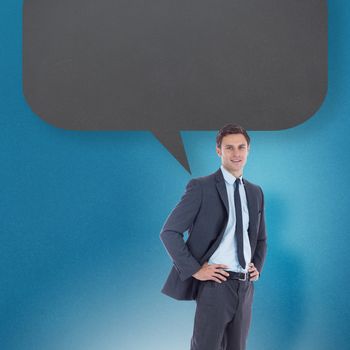 Smiling businessman with hands on hips with speech bubble against blue background with vignette